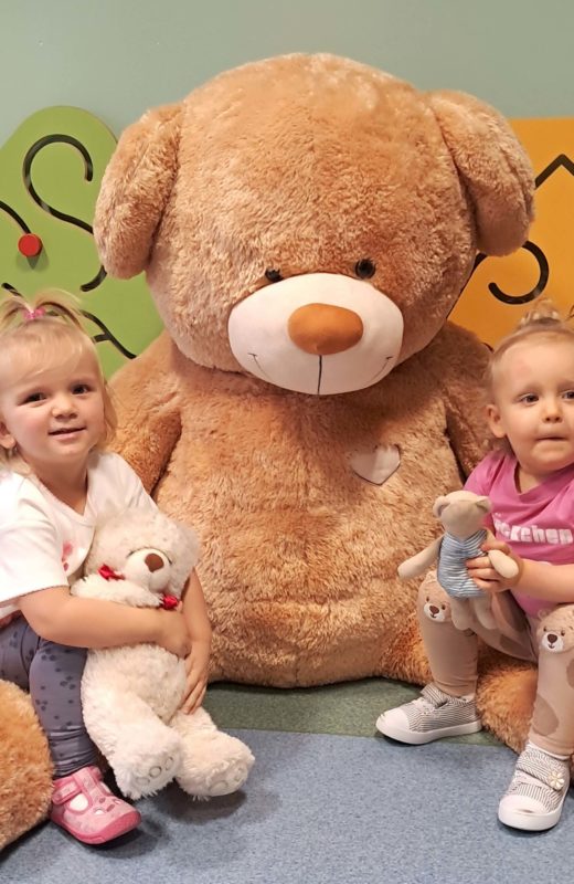Dziewczynki siedzą na dużym pluszowym misiu